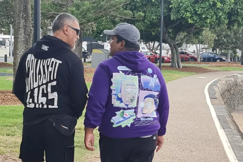 A young disabled man is walking along a beach path his his care provider