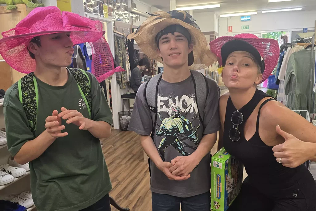 Two participants are trying on hats at the local costume store with their care provider