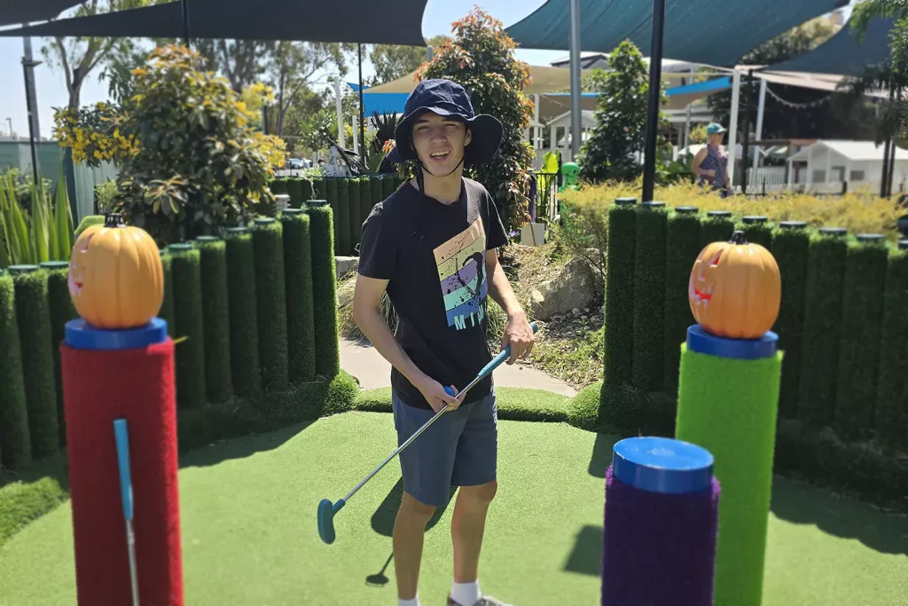 A young man with a disability is playing putt putt golf