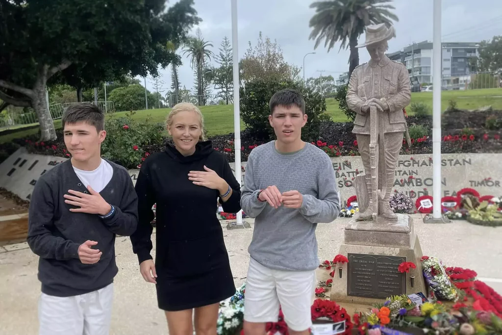 Two young participants are standing besides an Anzac memorial with their care provider