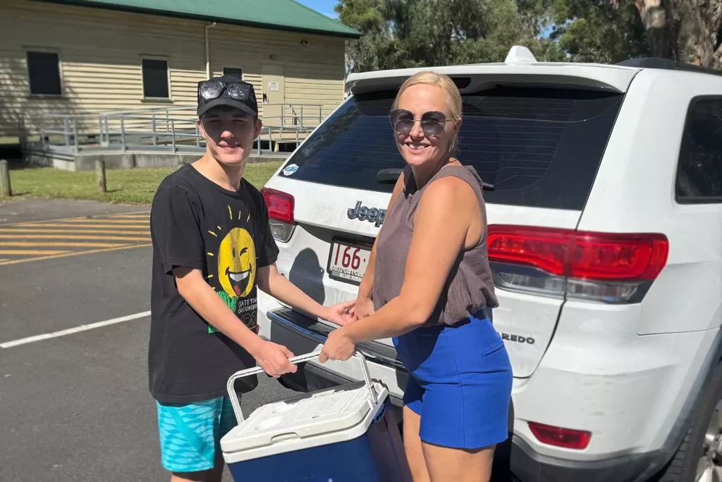 A young man with a disability is helping load an esky into the back of a car